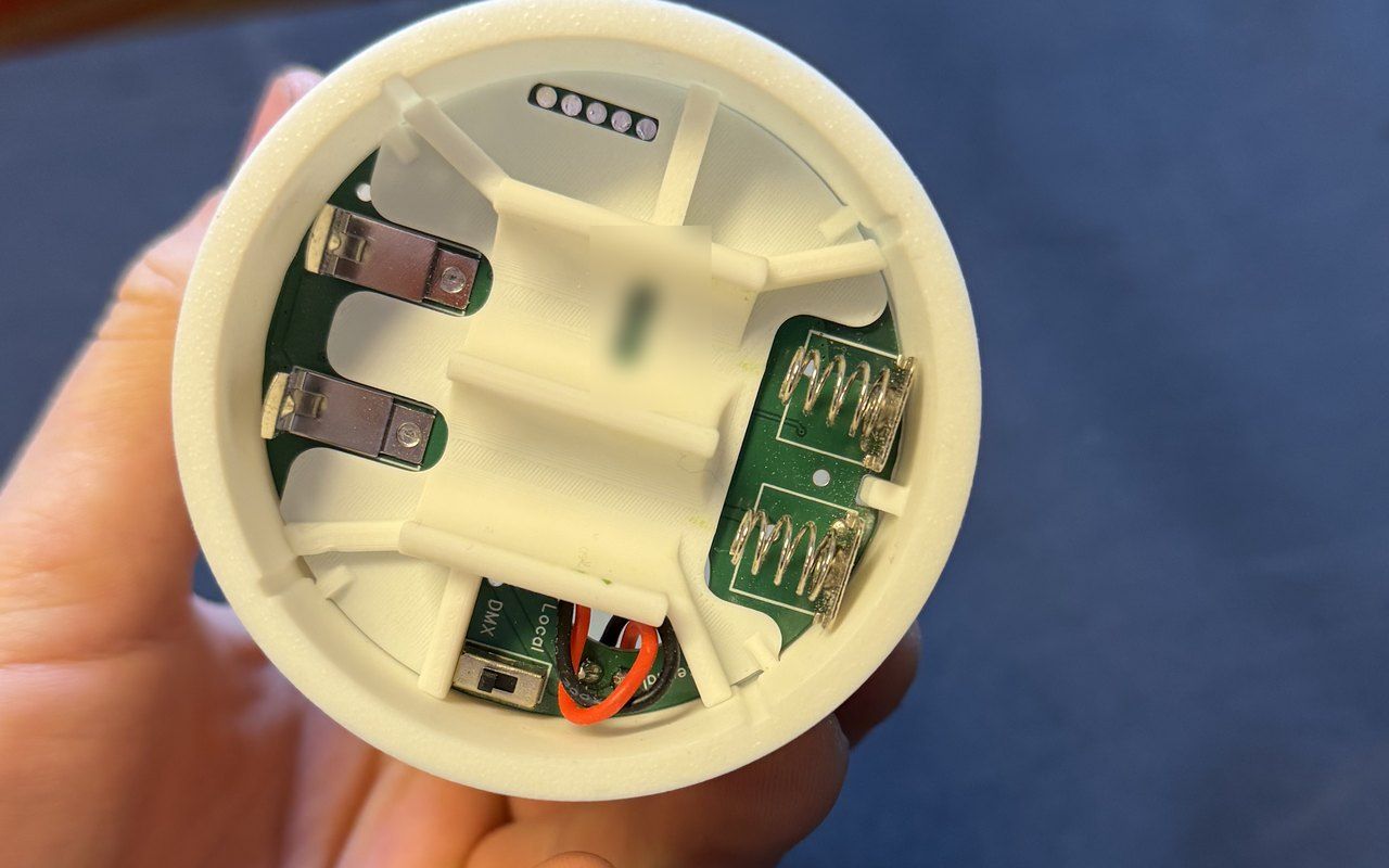 Undersiden av et kubbelys i en hånd: batteriholderen, kretskortet og bryteren for DMX eller lokal modus.